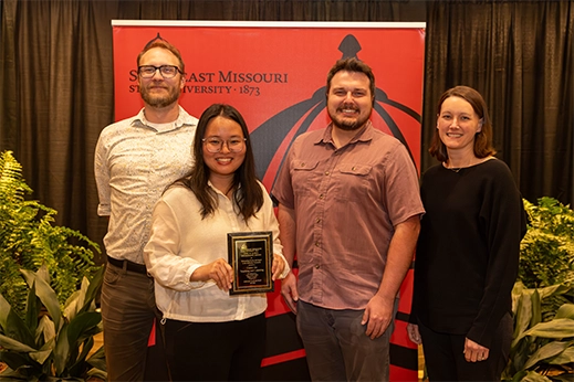 A group of professionals being presented a black plaque award in front of a red banner.