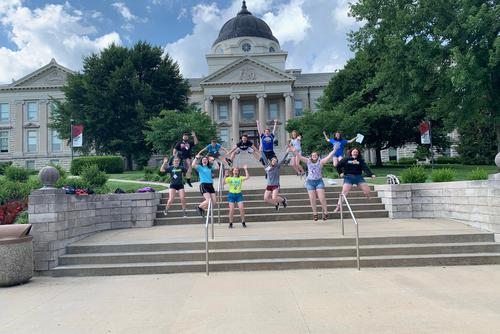 a group of students on the academic hall steps jumping as a group for a photo