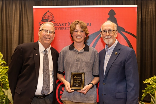A student is presented with a black plaque award in front of a red banner.
