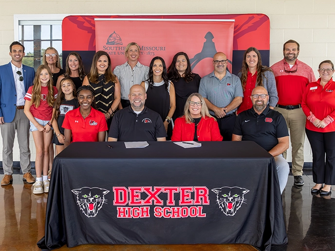 A group of professionals smiled behind a black-clothed table in front of a red banner.