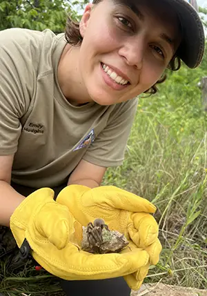 A photo of Emily Hudgins, Fulbright scholarship recipient smiling while holding a spider in her hands.