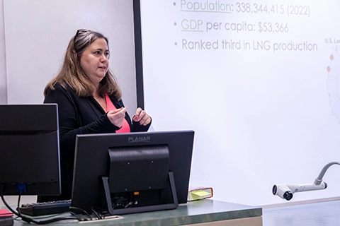 A professor gives a lecture in front of a projector screen. 