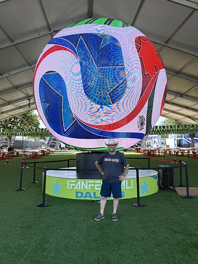 A photo of SEMO alumnus Mark Lee standing in front of the 36-foot tall LED sphere wearing a SEMO Alum t-shirt.