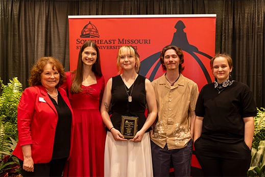 A student is presented with a black plaque award in front of a red banner.