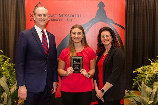 A student is presented with a black plaque award in front of a red banner.