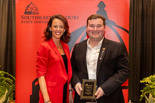 A student is presented with a black plaque award in front of a red banner.