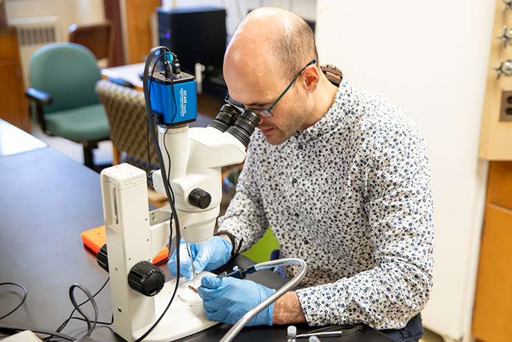 SEMO biology professor Lucas Kirschman wearing blue nitrile gloves looking into a microscope in his lab.