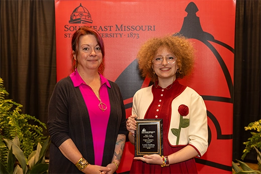 A student being presented a black plaque award in front of a red banner.