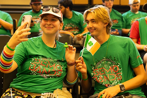 Two students in green shirts pose for a selfie.