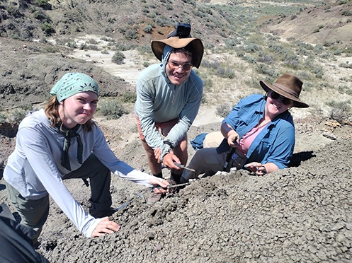 Three SEMO students smiling at the camera while looking for fossils in Montana at the PaleoX Field School.