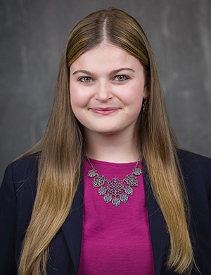 A professional headshot of a young woman in a fuschia blouse and dark blazer.