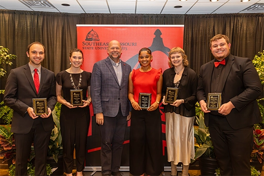 Students are presented with black plaque awards in front of a red banner.