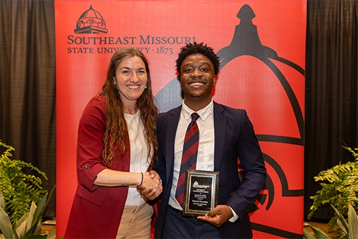 A student is presented with a black plaque award in front of a red banner.