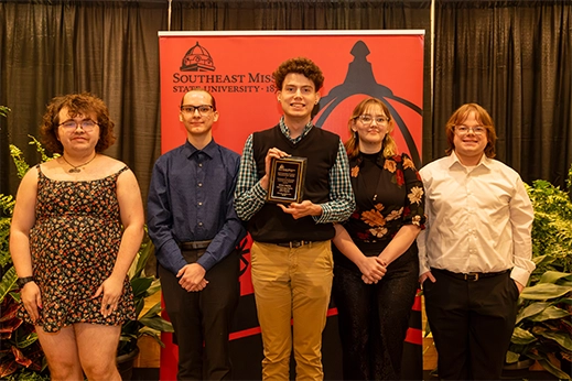Students are presented with a black plaque award in front of a red banner.
