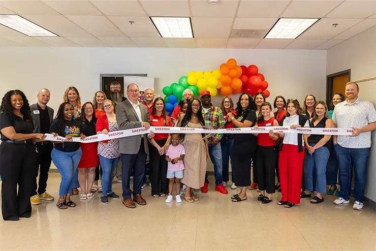 A photo of people gathered around a ribbon at the Future Leaders Learning Academy ribbon cutting ceremony.
