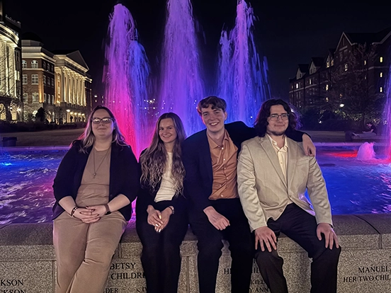 Students sit near a fountain in the evening at an event.