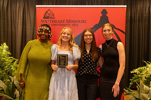 Students are presented with a black plaque award in front of a red banner.