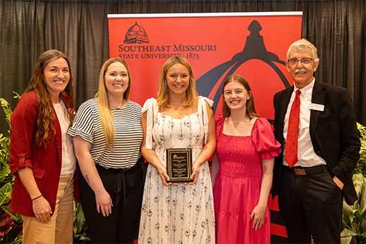 Students are presented with a black plaque award in front of a red banner.