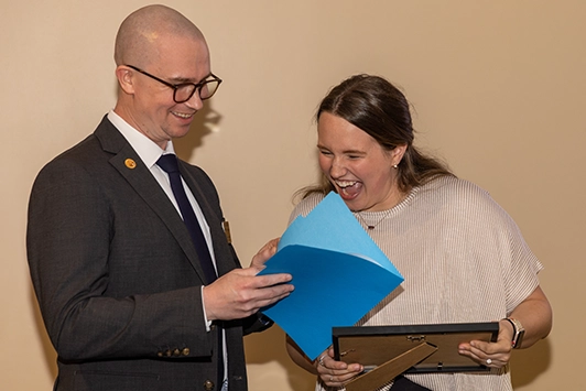 A young woman smiles with a man presenting her an award.