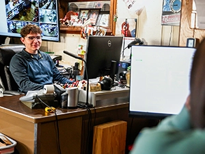 A young man works at a busy desk.