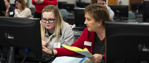 An academic advisor points to a computer screen while helping a student register for classes at First STEP.