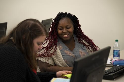 A student sits at a computer with an academic advisor to plan a class schedule.