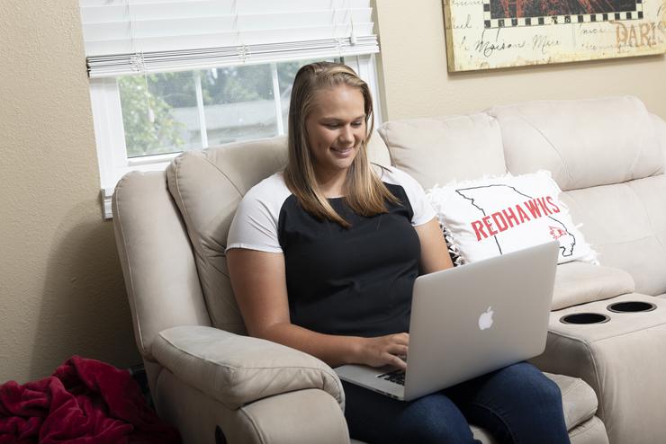  A student works on their laptop while sitting on a couch in their home. 