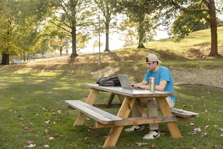 A student works on their assignments while enjoying time outside.  