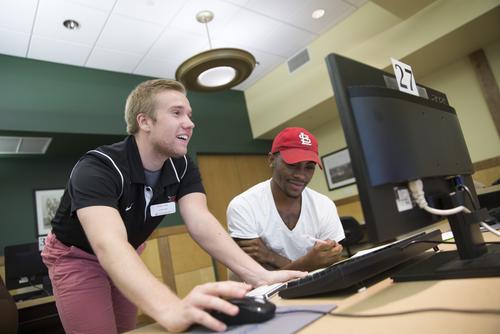 An academic advisor helps a student register for classes on the computer.