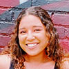 portrait of Mackenzie Wright posing in front of a brick wall, hands on hips and smiling