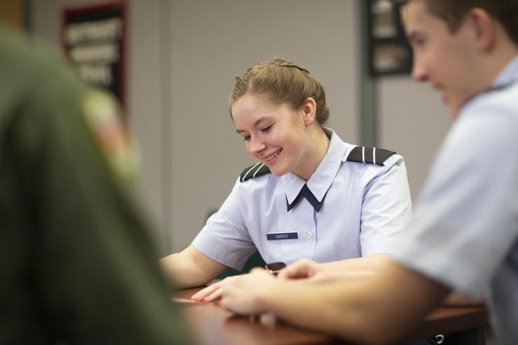 An in uniform ROTC student smiles while studying in the library. 