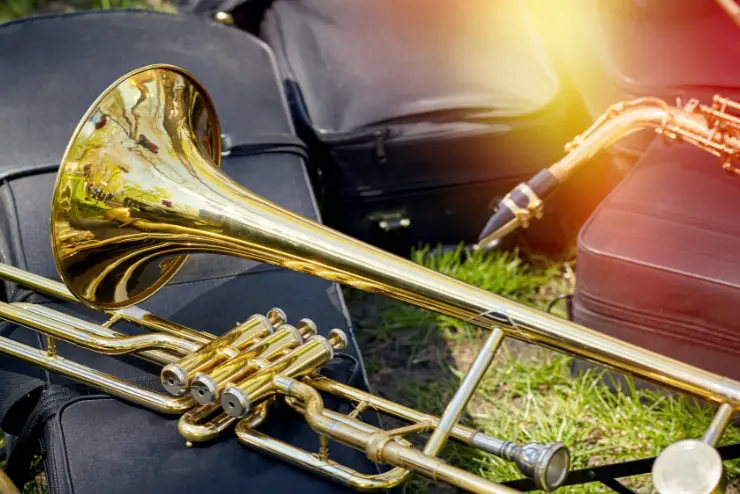 A close up of a a trombone laying on various instrument cases on the grass.