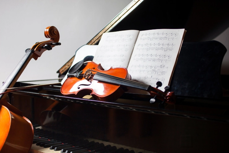 Violin resting on top of a grand piano against sheet music. A bass leans against the piano in front of the violin