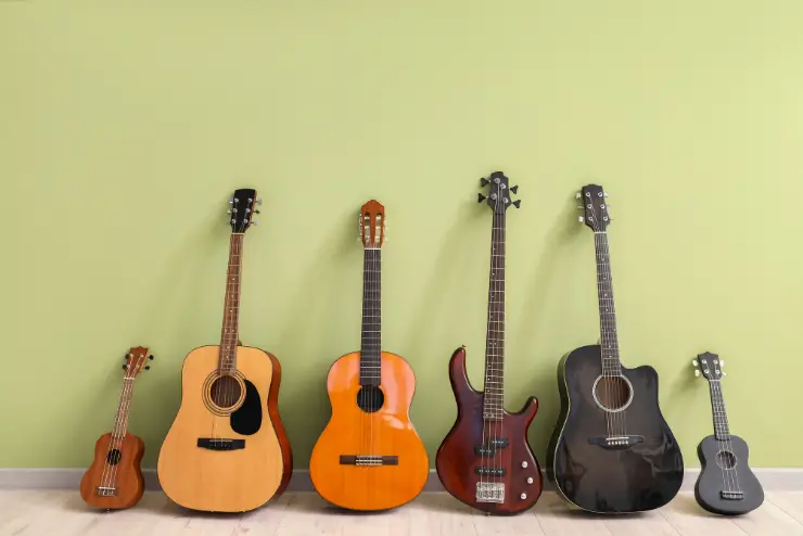 Five acoustic and one electric guitar propped up against a light green wall