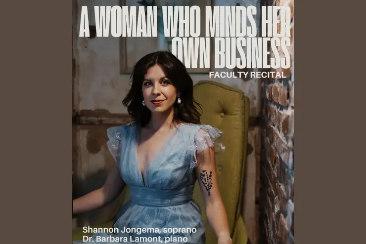 A woman in a blue dress with white earrings and a flower tattoo sitting in a yellow chair inside an old building by a brick wall