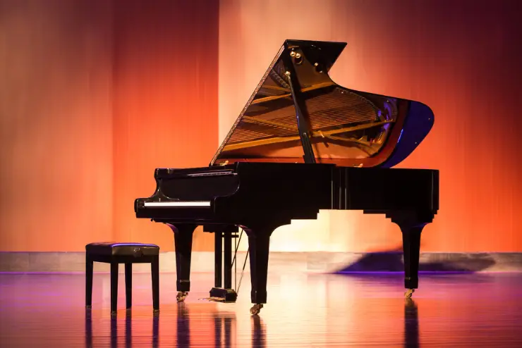 A grand piano and its seat is on a stage with orange and pink lighting