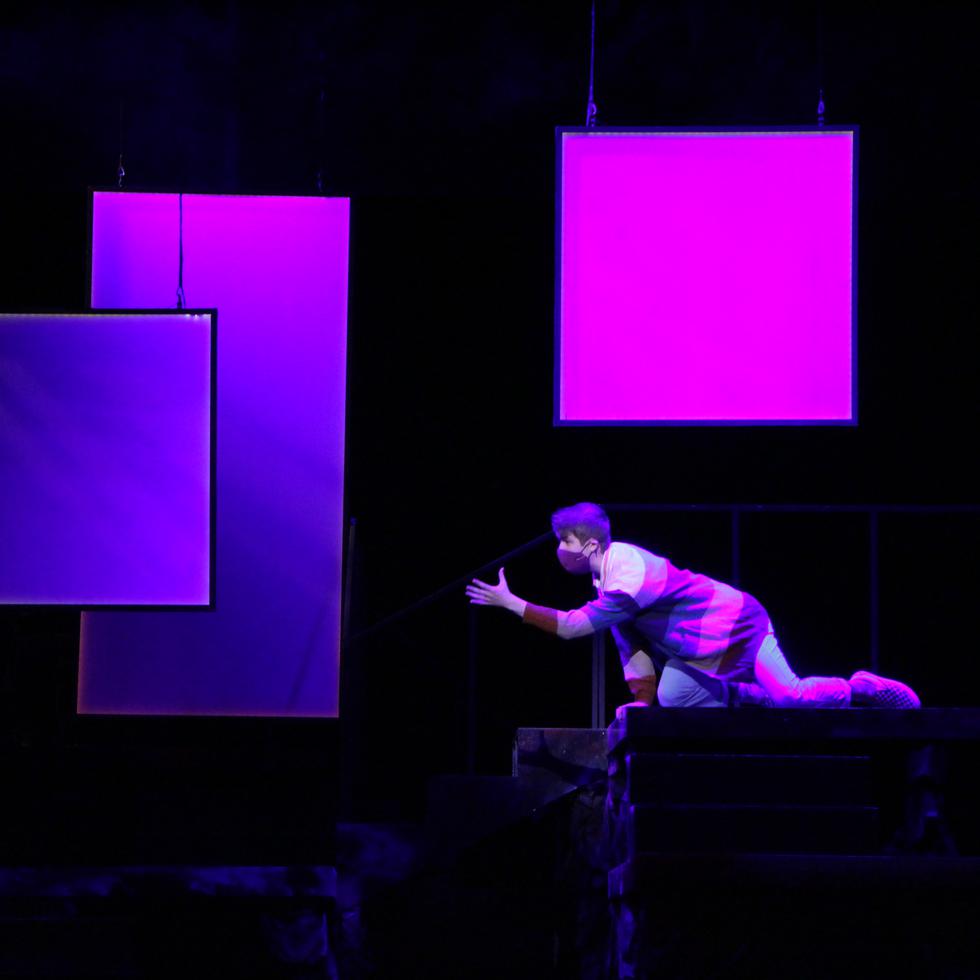 a student performs on stage against a dark background with white screens light with pink and purple lights