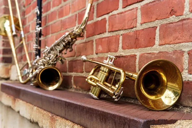 A trumpet, saxophone, clarinet, and trombone rest against a brick wall