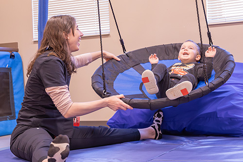 A communication disorders student pushes a little boy on an indoor swing.