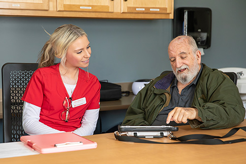 A Southeast nurse talks with an older client over a communication device.