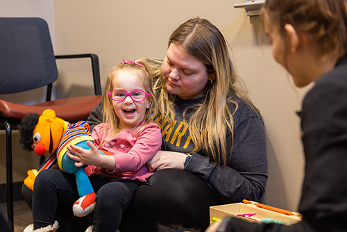 A communications disorders student holds a little girl playing with a Sesame Street doll at the Center for Speech and Hearing.