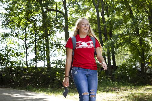 A student wearing a red SEMO shirt smiles as they walk down Cardiac Hill.