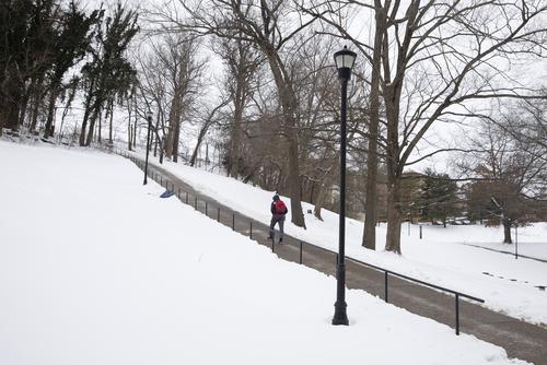 A student walks up the concrete pathway of Cardiac Hill with the ground covered in snow. 