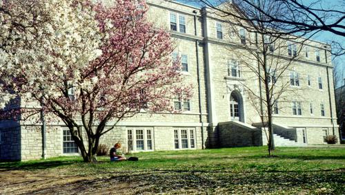A student sits outside under a tree in front of Cheney Hall.
