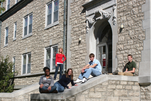 A group of students sits on the stairs and rails outside Cheney Hall.