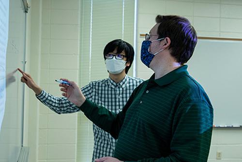 Dr. Dan Daly works with an early college student on a whiteboard.