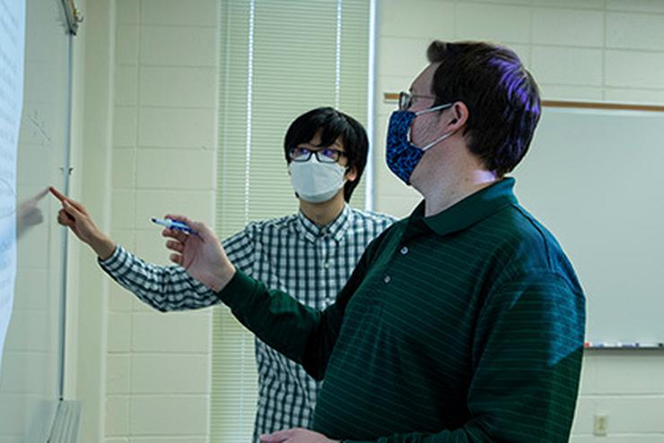 Dr. Dan Daly works with an early college student on a whiteboard.