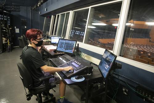 student seated at console in sound and lighting booth working on a sound board