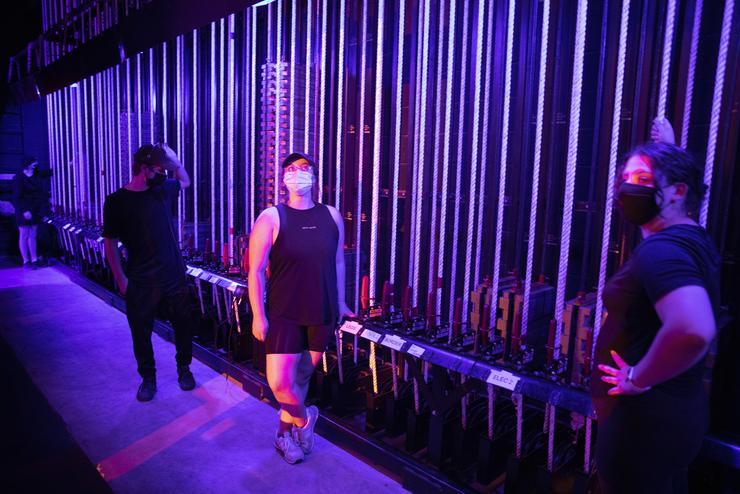 Three students wait in the wings beside a long row of ropes and pulleys.
