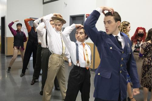 group of students stands in a hallway backstage in costume, practicing a song and dance number